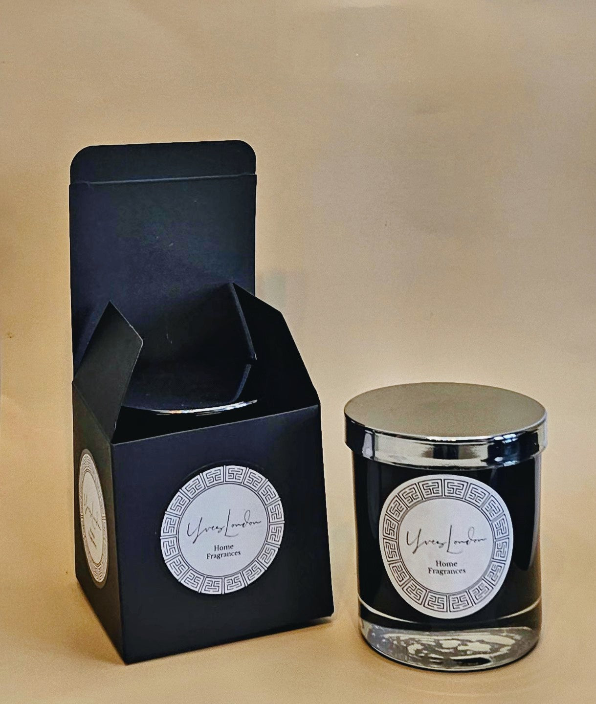 Candle in a sleek black jar with silver lid, and black box. Neutral background